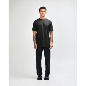 A black unisex short sleeve t-shirt worn with light blue baggy jeans and black sneakers. The model poses against a plain background.