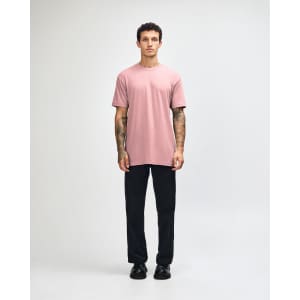 A model wearing a pink unisex CVC short sleeve T-shirt and black cargo pants, featuring a logo.