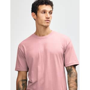 A model wearing a unisex short sleeve t-shirt in a soft pink colour. The shirt features a logo on the sleeve.