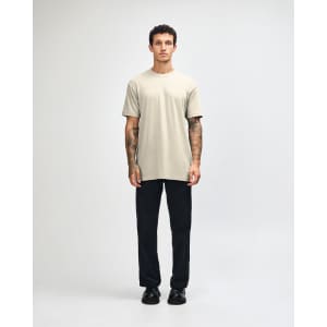 A unisex short sleeve T-shirt in beige, paired with black cargo pants, featuring a logo on the shirt.