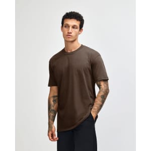 A unisex short sleeve T-shirt in brown, displayed on a model standing against a plain background. It features a logo.