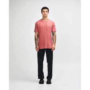 A unisex short sleeve t-shirt in rust colour, paired with black cargo pants. The model is standing with one hand in his pocket.