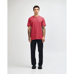 A unisex CVC short sleeve t-shirt in red, paired with black cargo pants. The model displays a casual pose.