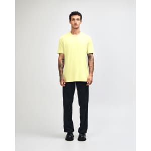 A man wearing a bright yellow unisex short sleeve t-shirt and black baggy pants, with sneakers.
