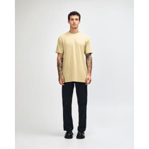 A unisex short sleeve T-shirt in a light khaki colour, worn with black cargo pants, features a logo.