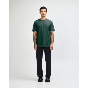 A green unisex CVC short sleeve T-shirt displayed on a model wearing black cargo pants and sneakers.