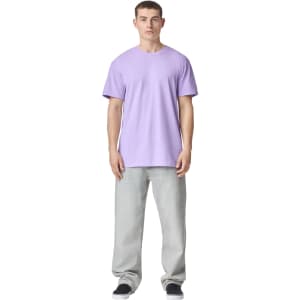 A model stands in a lavender unisex CVC short sleeve T-shirt paired with light grey trousers. The shirt has a logo.