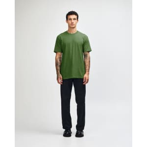 A unisex short sleeve T-shirt in green, worn with black cargo pants. The model is standing with a relaxed pose.
