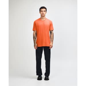 A model wearing an orange unisex CVC short sleeve t-shirt paired with black cargo trousers and sneakers.