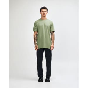 A model wearing a green unisex short sleeve T-shirt and black cargo pants, standing in a neutral setting.