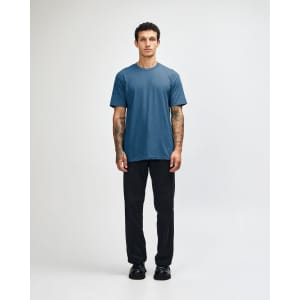 A unisex CVC short sleeve t-shirt in a blue shade, paired with black cargo pants. The model stands casually.