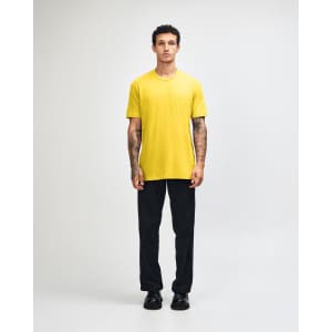 A model wearing a yellow unisex short sleeve T-shirt with black cargo pants and green and white shoes, featuring a logo.