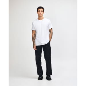 A young man wearing a plain white unisex short sleeve t-shirt and loose blue jeans, standing against a white background.