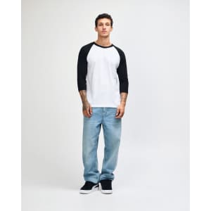 A unisex raglan T-shirt in white with black sleeves, paired with dark cargo pants. The model stands against a plain background.