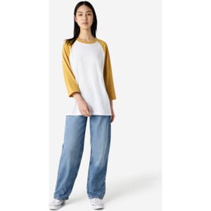 A unisex raglan t-shirt with white body and mustard yellow sleeves, paired with loose blue jeans.