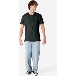 A dark green unisex Henley T-shirt displayed on a model wearing light blue jeans and black sneakers.
