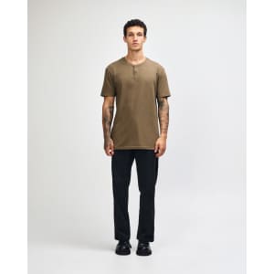 A unisex henley T-shirt in olive green, paired with light blue baggy jeans, displayed on a model.