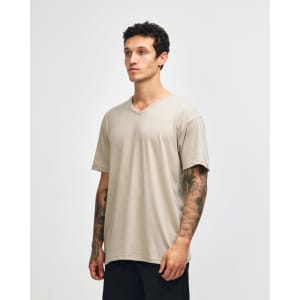 A unisex V-neck T-shirt in a beige colour, displayed on a model from the side. The shirt has a logo.