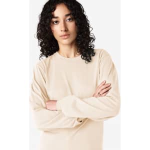 A long sleeve t-shirt in a light beige colour on a model with curly hair, featuring a small logo.