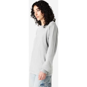 A grey long sleeve t-shirt with a relaxed fit, featuring a logo on the front. The model has curly hair.