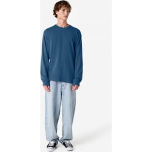 A person wearing a blue long sleeve T-shirt with a relaxed fit, paired with light blue jeans and black shoes.