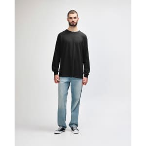 A long sleeve t-shirt in dark grey worn by a model, paired with black trousers and sneakers.