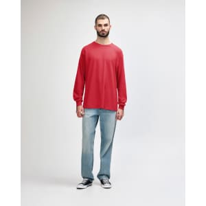A male model wears a red long-sleeve t-shirt paired with black jeans and sneakers. The shirt features a logo.