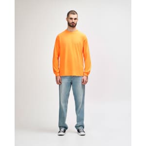 An orange long sleeve t-shirt worn by a standing male model, paired with black pants and sneakers.