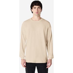 A long sleeve t-shirt in beige worn by a model, featuring a relaxed fit and a branding logo.