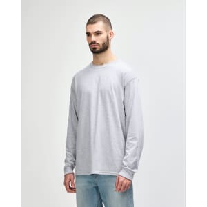 A long sleeve grey t-shirt displayed on a model wearing dark pants and white sneakers, featuring a logo.