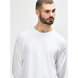A white long sleeve t-shirt on a model, showcasing a classic fit and simple design. The shirt features a logo.