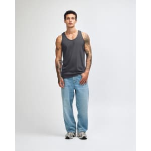 A unisex fine jersey tank in grey, worn with black loose-fitting pants and white sneakers. The tank features a logo.
