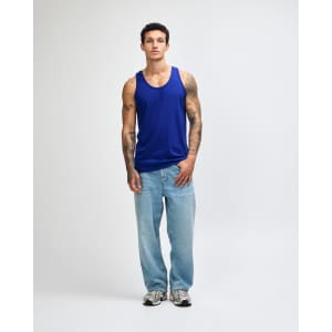 A unisex fine jersey tank in blue, paired with black cargo pants and green and white sneakers. Features a branding logo.