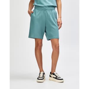 A pair of teal unisex gym shorts with an elastic waistband and side pockets, worn with white sneakers and socks.