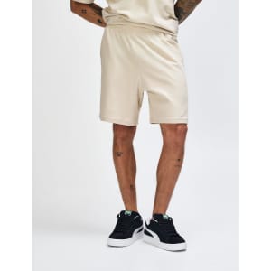 Beige unisex gym shorts with an elastic waistband and side pockets, worn with white sneakers and grey socks.