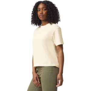 A light beige boxy t-shirt with short sleeves, modelled by a woman with curly hair, featuring a logo.