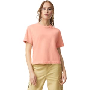 A boxy women's T-shirt in a soft coral colour with short sleeves and a round neckline. It has a logo on it.