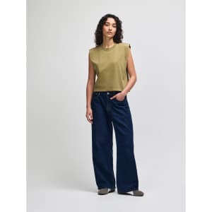 A woman is wearing an olive green muscle T-shirt paired with light blue baggy jeans. The outfit has a casual style.