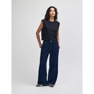 A grey women's muscle t-shirt paired with light blue baggy jeans and black and white sneakers.