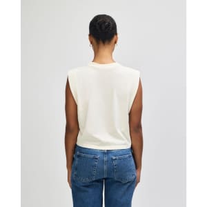 A women's muscle T-shirt in cream, featuring a sleeveless design and a relaxed fit. The shirt has a visible logo.