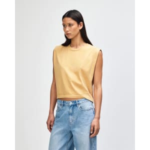 A mustard yellow women's muscle T-shirt with a relaxed fit and short sleeves. The model has curly hair and wears high-waisted jeans.