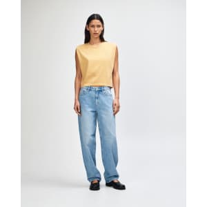 A mustard women's muscle T-shirt paired with light blue baggy jeans, featuring a logo.