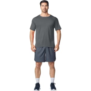 A grey Gildan Performance adult t-shirt displayed on a model, paired with dark sports shorts and shoes.