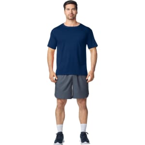 A man stands in a navy blue Gildan Performance adult t-shirt and grey shorts, wearing athletic shoes.