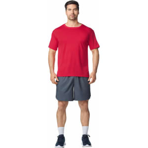 A man wearing a red Gildan Performance adult t-shirt and grey shorts, standing in a relaxed pose.
