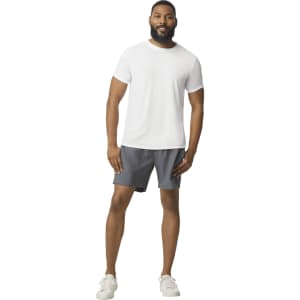 A man wearing a white Gildan Performance adult T-shirt and grey shorts, standing casually and smiling.