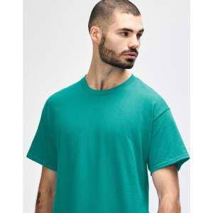 A turquoise Gildan Heavy Cotton Adult T-Shirt on a model, featuring a simple design and a logo.