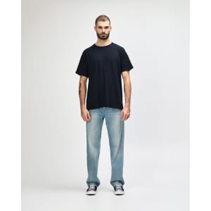 A black Gildan Heavy Cotton Adult T-Shirt worn by a model, paired with dark jeans and sneakers.