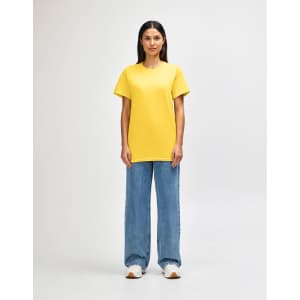 A yellow Gildan Heavy Cotton adult T-shirt worn by a male model, alongside black pants and sneakers.