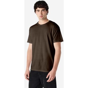 A man stands wearing a brown Gildan Heavy Cotton Adult T-Shirt. The shirt has a logo on it and a relaxed fit.